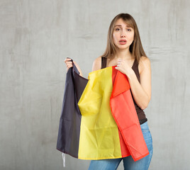 Portrait of sad unhappy young woman holding national flag of Belgium, posing against gray studio background