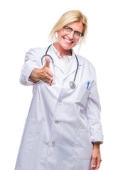 Wall Mural - Middle age blonde doctor woman over isolated background smiling friendly offering handshake as greeting and welcoming. Successful business.