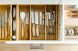 The photo is taken from above a kitchen cabinet with drawers for knives, spoons and other utensils, separated by functionality and organized for ease of use in a modern style.