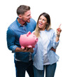 © Krakenimages.com - Young couple in love holding piggy bank over isolated background very happy pointing with hand and finger to the side