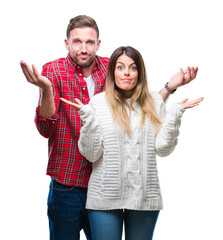 Sticker - Young couple in love wearing winter sweater over isolated background clueless and confused expression with arms and hands raised. Doubt concept.