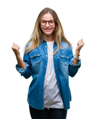 Young beautiful blonde woman wearing glasses over isolated background celebrating surprised and amazed for success with arms raised and open eyes. Winner concept.