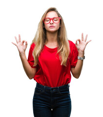 Sticker - Young beautiful blonde woman wearing glasses over isolated background relax and smiling with eyes closed doing meditation gesture with fingers. Yoga concept.