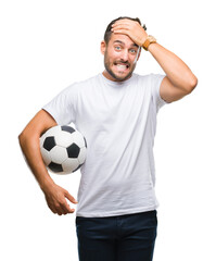 Poster - Young handsome man holding soccer football ball over isolated background stressed with hand on head, shocked with shame and surprise face, angry and frustrated. Fear and upset for mistake.