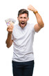 Young handsome man holding stack of dollars over isolated background annoyed and frustrated shouting with anger, crazy and yelling with raised hand, anger concept