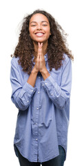 Wall Mural - Young hispanic business woman praying with hands together asking for forgiveness smiling confident.
