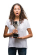 Young hispanic woman holding trophy scared in shock with a surprise face, afraid and excited with fear expression