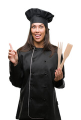 Poster - Young hispanic cook woman wearing chef uniform surprised with an idea or question pointing finger with happy face, number one