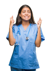 Wall Mural - Young arab doctor surgeon woman over isolated background smiling crossing fingers with hope and eyes closed. Luck and superstitious concept.