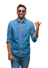 Wall Mural - Adult hispanic man wearing sunglasses over isolated background smiling with happy face looking and pointing to the side with thumb up.