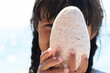 child playing peekaboo with large oval stone on sunny beach