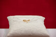 golden wedding rings on white embroidered pillow against red background