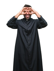 Canvas Print - Adult hispanic catholic priest man over isolated background doing ok gesture like binoculars sticking tongue out, eyes looking through fingers. Crazy expression.