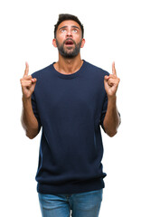 Poster - Adult hispanic man over isolated background amazed and surprised looking up and pointing with fingers and raised arms.