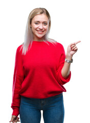 Wall Mural - Young blonde woman wearing winter sweater over isolated background with a big smile on face, pointing with hand and finger to the side looking at the camera.