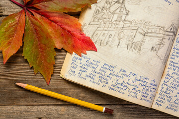 Wall Mural - Vintage expedition journal on a rustic picnic table with a colorful leaf. Travel log from paddling trip across Poland in 1974 - handwriting and drawing in pencil.