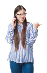 Sticker - Young Chinese woman over isolated background speaking on the phone pointing and showing with thumb up to the side with happy face smiling