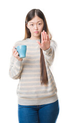 Canvas Print - Young Chinese woman over isolated background driking cup of coffee with open hand doing stop sign with serious and confident expression, defense gesture