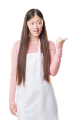 Wall Mural - Young Chinese shop owner woman over isolated background wearing white apron pointing and showing with thumb up to the side with happy face smiling