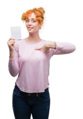 Wall Mural - Young redhead woman holding blank notebook with surprise face pointing finger to himself