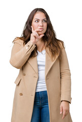 Wall Mural - Beautiful plus size young woman wearing winter coat over isolated background with hand on chin thinking about question, pensive expression. Smiling with thoughtful face. Doubt concept.