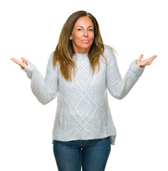Wall Mural - Beautiful middle age adult woman wearing winter sweater over isolated background clueless and confused expression with arms and hands raised. Doubt concept.