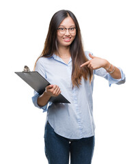 Sticker - Young asian business woman holding clipboard over isolated background with surprise face pointing finger to himself