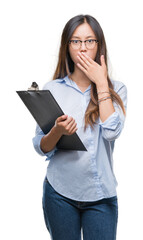 Canvas Print - Young asian business woman holding clipboard over isolated background cover mouth with hand shocked with shame for mistake, expression of fear, scared in silence, secret concept