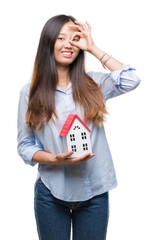 Poster - Young asian woman real state agent holding house isolated background with happy face smiling doing ok sign with hand on eye looking through fingers