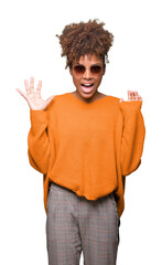 Wall Mural - Beautiful young african american woman wearing sunglasses over isolated background celebrating crazy and amazed for success with arms raised and open eyes screaming excited. Winner concept