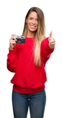 Poster - Beautiful young woman holding vintage camera happy with big smile doing ok sign, thumb up with fingers, excellent sign