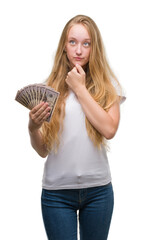 Poster - Blonde teenager woman holding dollars serious face thinking about question, very confused idea