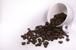 Rozsypane ziarna aromatycznej kawy z filiżanki na jasnym tle