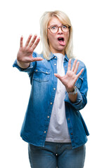 Wall Mural - Young beautiful blonde woman wearing glasses over isolated background afraid and terrified with fear expression stop gesture with hands, shouting in shock. Panic concept.