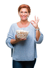 Canvas Print - Atrractive senior caucasian redhead woman eating popcorn over isolated background with a happy face standing and smiling with a confident smile showing teeth