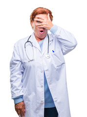 Canvas Print - Senior caucasian doctor woman wearing medical uniform over isolated background peeking in shock covering face and eyes with hand, looking through fingers with embarrassed expression.