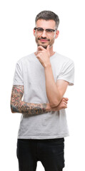 Wall Mural - Young tattooed adult man looking confident at the camera with smile with crossed arms and hand raised on chin. Thinking positive.