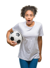 Poster - Young beautiful afro american holding soccer football ball over isolated background scared in shock with a surprise face, afraid and excited with fear expression