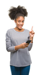 Canvas Print - Young afro american woman texting using smartphone over isolated background surprised with an idea or question pointing finger with happy face, number one