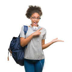 Sticker - Young afro american student woman wearing headphones and backpack over isolated background amazed and smiling to the camera while presenting with hand and pointing with finger.