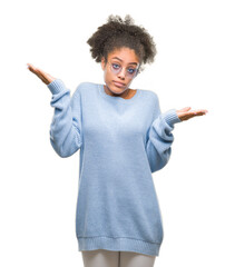 Wall Mural - Young afro american woman wearing glasses over isolated background clueless and confused expression with arms and hands raised. Doubt concept.