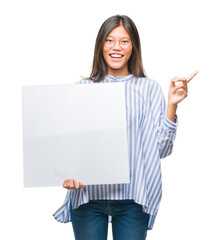 Sticker - Young asian woman over isolated background holding blank banner very happy pointing with hand and finger to the side