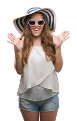 Sticker - Young blonde woman wearing sunglasses and summer hat very happy and excited, winner expression celebrating victory screaming with big smile and raised hands