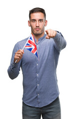 Wall Mural - Handsome young man holding a flag of United Kingdom pointing with finger to the camera and to you, hand sign, positive and confident gesture from the front