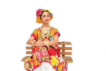 Mexican girl with a floral dress from Oaxaca Mexico, hidden in a red background with braided flowers and gold necklaces, for Mexican culture dance