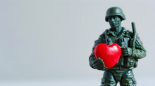 Green Plastic Toy Soldier With A Red Heart In His Hand On A White Background.
