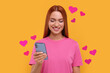 Long distance love. Woman chatting with sweetheart via smartphone on golden background. Hearts flying out of device and swirling around her