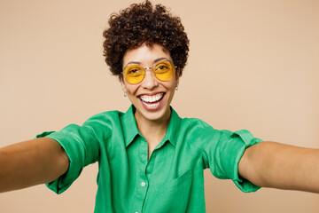 Poster - Close up young woman of African American ethnicity wear green shirt casual clothes glasses doing selfie shot pov on mobile cell phone isolated on plain light beige background studio Lifestyle concept