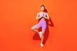 © ViDi Studio - Full body young fitness trainer woman sportsman wear purple top clothes train in home gym hold hands in yoga om aum gesture meditate isolated on plain orange background. Workout sport fit abs concept.