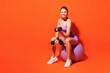 Full body happy young fitness trainer woman sportsman wear top shorts purple clothes train in home gym sit on fit ball hold dumbbells isolated on plain orange background Workout sport fit abs concept